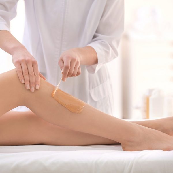 Beautician waxing female legs in spa center